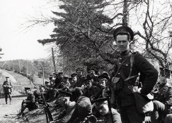 Photographie en noir et blanc d’un groupe de soldats debout ou assis au sommet d’une colline le long de la route.