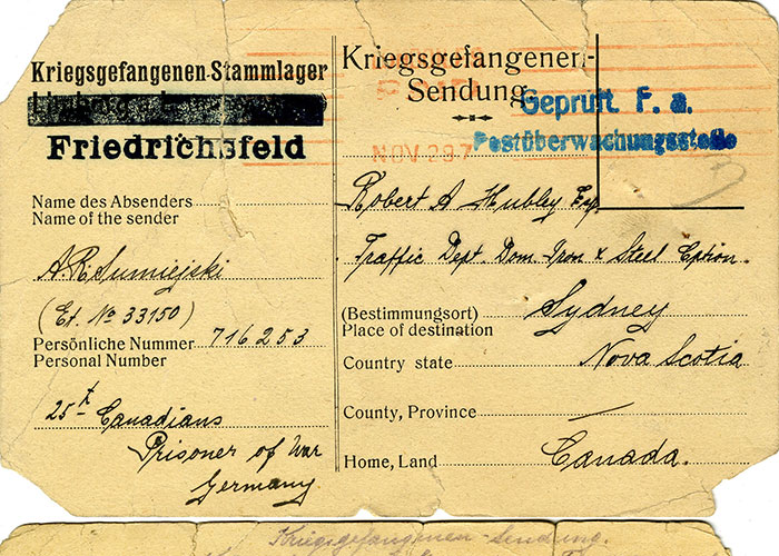 Image composite sépia d’une carte postale, avec le recto de la carte en haut et son verso au bas de l’image. Le devant de la carte postale porte des marques gouvernementales et postales en encre bleue et rouge, une adresse écrite à la main et une adresse caviardée du camp de prisonniers de guerre, le tout à l’encre noire. Au verso, on voit une écriture manuscrite au crayon.