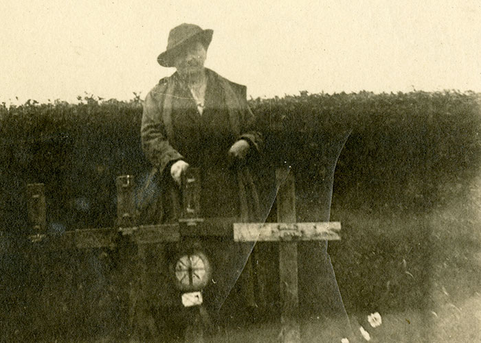 Photographie en couleur sépia d’une femme debout à l’extérieur à côté de plusieurs croix tombales en bois.