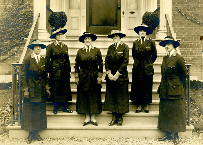Sepia photograph of six nurses from the Royal Victoria Hospital standing in front of a brick building in Montreal. They are wearing matching dark-coloured woolen nurses' uniforms with ties and wide-brimmed hats.