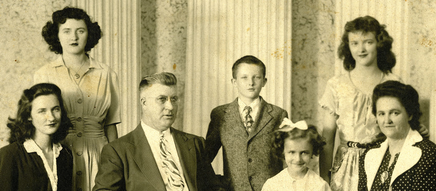 Sepia portrait of a family in a studio; there are two parents and five children.