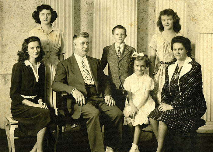 Sepia portrait of a family in a studio; there are two parents and five children.