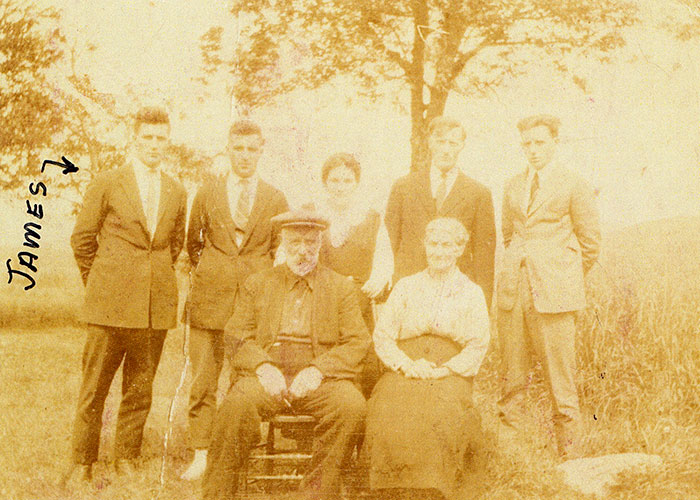 Sepia photograph of a family taken outdoors. The two elderly parents are sitting on chairs in the foreground, with five children standing behind them. Someone has written "James" in black pen ink next to James Murphy, standing at left of the image.