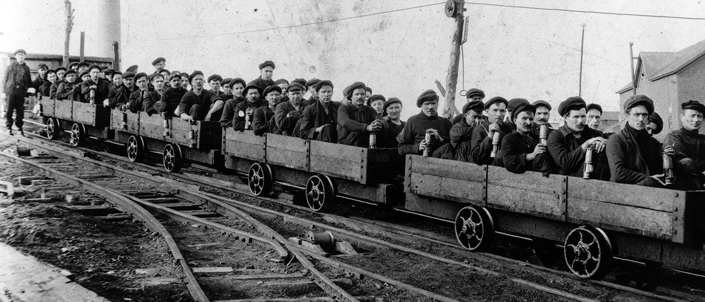 Image is a black and white photograph of men on a coal mining rake.